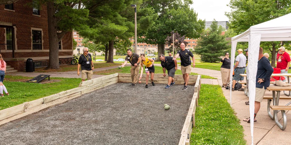 A group of Michigan Tech alumni play bocce ball on campus in Houghton, Michigan, as others watch.