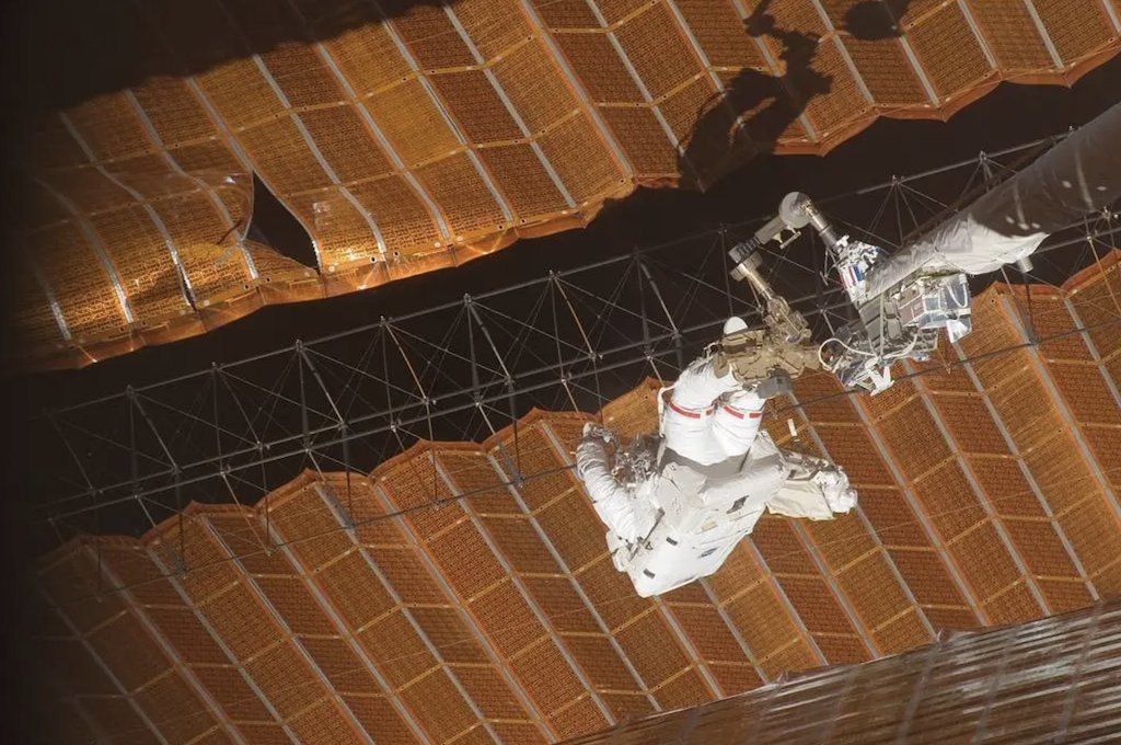 AstroPeggy's tweet photo. The original solar arrays on the International Space Station are among the most impressive engineering feats in space. They were the @Space_Station's primary power source until the more recent addition of the roll-out-solar arrays. Despite their size (115 feet long) , they're very delicate and incredibly thin. The first month I commanded the Space Station we were tasked with moving the P6 truss element from its temporary location to its final position at the end of the port truss. The first half of the wing deployed nominally from a small blanket box that the array had been folded within. While commanding the second half of the wing, we saw it began to tear. We immediately aborted the deployment, but were left with about a 6-foot tear way beyond anything the robotic arm alone could reach. It was a bit of a limbo situation: we didn't want to continue and worsen the tear, but we also had no way to refold it into the box. With limited supplies available, the ground crew suggested we make some cufflinks out of metal and cut wire to repair it as best we could. And then they designed and tested the reach in the virtual reality lab of the Shuttle inspection arm attached to the Station big arm to get a crewmember close enough to install the cufflinks. The ground team heroes came up with a solution to what seemed to be an impossible problem, and even with the tear the array produced 97% of its original power!
