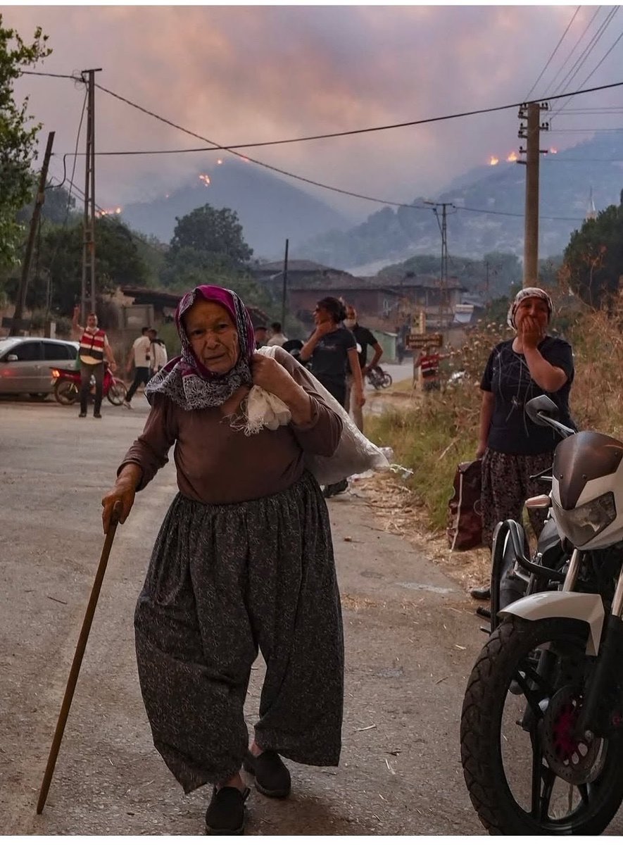 nrtn3545's tweet photo. Arkada orman alev alev yanıyor.  Elinde değneğiyle güçlükle yürüyen yaşlı bir kadın, omzunda zar zor taşıdığı son eşyasıyla. Çaresizlik! Fotoğraf çok şey anlatıyor ama anlamak isteyene...
Fotoğrafın her bir karesinde bir öykü var. Neresinden tutsan damarların patlar!
Ah!
#yangın https://t.co/JdYsgE8GCM