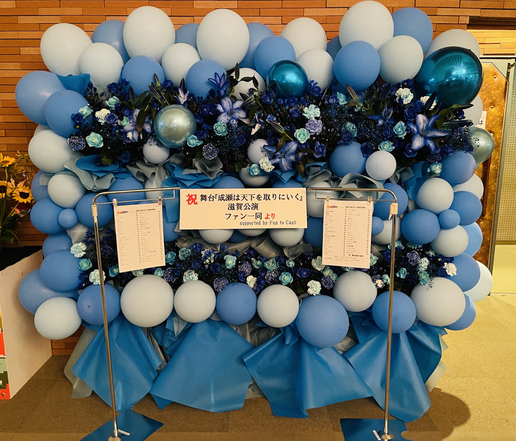 yeltama's tweet photo. 舞台『#成瀬は天下を取りにいく』滋賀公演お祝い企画の報告とお礼
➡️https://t.co/8W0sgwHO6T

大千穐楽を迎える大津公演の、楽屋が企画にご参加いただいた皆様からのメッセージで、ロビーが琵琶湖ブルーの特大バルーンフラワースタンドで彩られました✨時間をかけて色水を吸収した特製のお花です💐

アンケート欄にお寄せいただいた声もご紹介させてください。

---
「こういう企画は初めて知りました。とても素敵な手法だと思います。またあれば是非参加したいです」

「ファンもいっしょに盛り上げられるとても素敵な企画なので機会があればこれからも参加させてもらいたいです」

「自分1人では出来ない事をみんなで気持ちを届ける企画素敵ですね」

「フラワースタンドを送った経験がなかったので、こういった企画を通して参加できてよかったです！」

「フラワースタンドの類は華やかだけど贈る方も贈られる方も意外と大変なことだと感じます。このような持ち寄り型は双方の事情も汲み取りやすく、いいなと思い参加いたしました！」

「この様なファン参加型の企画がある事を初めて知りました｡メッセージも届けていただけて嬉しいですありがとうございます^_^」

「値段も手頃で気持ちも伝えられていいと思う」

「このような素敵な企画に参加することができ非常に嬉しく思います。1人では難しいのでありがたいです」

「初めてこのような形で応援させていただきました。いつも出演者から素敵な思い出をもらってばっかりなので、このような形で応援する側が何か残せる経験ができる素敵な企画だと思いました」
---

まだまだ沢山のコメントをいただき紹介しきれないのですが、とても温かいメッセージから、
皆様が普段、作品や出演者の方達からステキな感情を受け取っていることがひしひしと伝わってきました。

私たち #ファンキャス も、いただいたお言葉を励みにこれからも皆様のお気持ちの架け橋になれれば幸いです。

企画にご参加いただいた皆様や、公演の主催者様のご協力も得て、一緒に華を添えさせていただくことができました。ありがとうございます。
あらためまして大千穐楽まで、おつかれ様でございました。

*引用元の投稿からは、大千穐楽のカーテンコールの映像が観られます👏👏👏