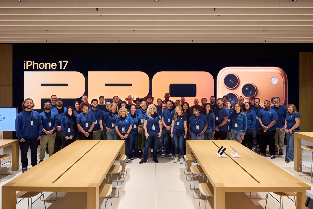 A group photo of the retail team at the all-new Apple Briarwood, posing in front of a large digital wall showcasing an ad for the iPhone 17 Pro.