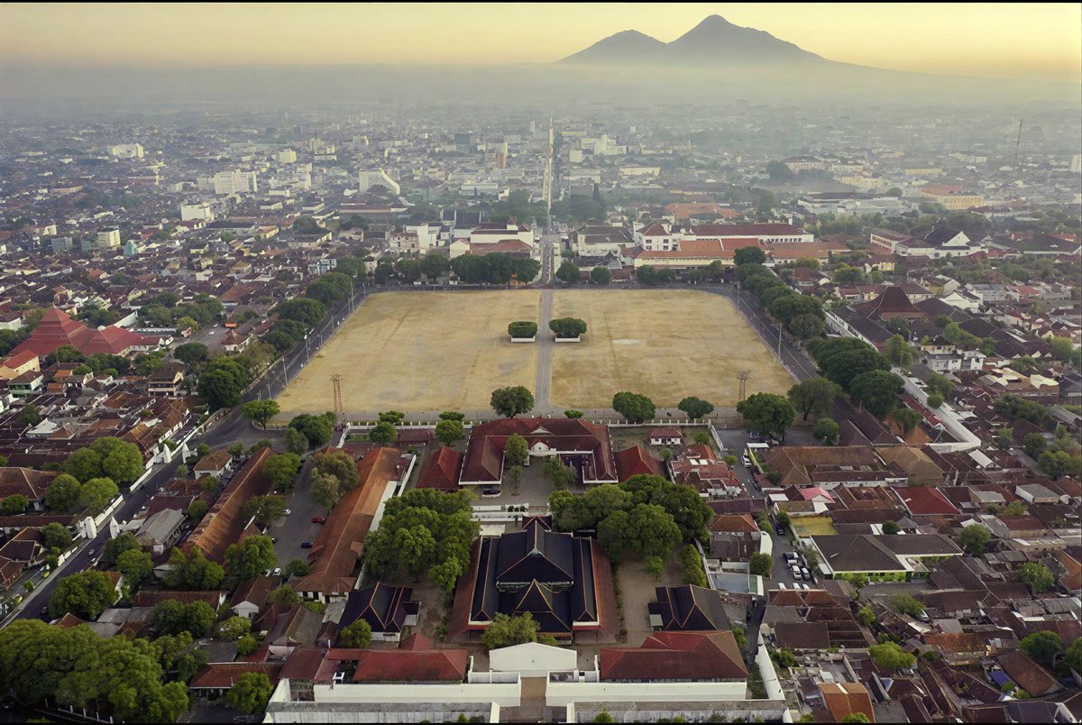 narachronicle's tweet photo. Banyak kota di Indonesia yang punya satu ruang publik dan bentuknya hampir selalu sama. Alun-alun, dan bentuknya hampir selalu persegi.

​Ini jelas bukan kebetulan belaka. Alun-alun tuh sebenarnya lahir dari cara pandang Jawa kuno soal pusat kekuasaan. Di depan keraton, biasanya dibuka sebuah lapangan luas berbentuk segi empat.

Bentuk itu sengaja dipilih karena ngasih kesan tertib, seimbang, dan gampang dikontrol. Dari sudut mana pun, ruang itu bisa diawasi dengan mudah. Dan dari sudut mana pun, orang bakal merasa lagi berdiri di tengah pusat kekuasaan.

​Di sebelah utara biasanya ada keraton atau pusat pemerintahan. Di selatan atau sekitarnya ada masjid. Lalu di sisi lainnya ada pasar atau ruang publik.

​Susunan kayak gini tuh bukan sekadar tata kota biasa. Ini adalah sebuah peta sosial. Siapa yang berkuasa di pusat, siapa yang ada di pinggiran, dan gimana caranya orang-orang harus bergerak di dalamnya.

​Pas kota-kota baru mulai tumbuh, pola ini terus ditiru. Bahkan di luar Pulau Jawa pun, banyak alun-alun yang tetep dibuat bentuk persegi karena model itu udah terlanjur dianggap sebagai standar ruang publik yang "resmi".

​Jadi yang sering kita liat sekarang bukan cuma sekadar lapangan kosong di tengah kota doang. Itu adalah sisa-sisa cara berpikir lama dalam mengatur dunia: bahwa pusat kekuasaan itu harus jelas, bentuknya harus teratur, dan ruangannya harus bisa dibaca sama siapa pun yang berdiri di dalamnya.

​Kadang tata kota yang kelihatannya paling biasa justru menyimpan cara berpikir yang paling tua.