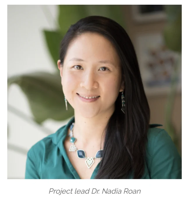 Project lead Dr. Nadia Roan. An East-Asian woman with dark brown, long straight hair is looking into the camera and smiling. She wears a turquoise button-up blouse with the collar open and a necklace with dark blue and turquoise gemstones.