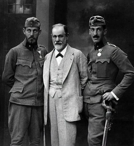 icardo8's tweet photo. FREUD SUS HIJOS Y LA GUERRA

La fotografía parece mostrar a un padre orgulloso junto a dos hijos uniformados. En realidad, conserva uno de los pocos momentos en que Sigmund Freud pudo comprobar personalmente que ambos seguían vivos.

La imagen fue tomada en Salzburgo en agosto de 1916. Junto a Freud aparecen Ernst y Martin, dos de sus tres hijos varones, vestidos como oficiales del ejército austrohúngaro y temporalmente alejados del frente.

El tercero, Oliver, también prestó servicio durante la Primera Guerra Mundial, aunque no aparece en el retrato.

Cuando el conflicto comenzó en 1914, Freud tenía 58 años y era demasiado mayor para ser movilizado. Como muchos intelectuales de Viena, recibió inicialmente la guerra con un entusiasmo patriótico que pronto terminaría resultándole difícil de reconocer.

Martin, su hijo mayor, acababa de completar sus estudios de Derecho. Al principio creyó que la guerra duraría poco y que él y sus hermanos quizá no serían llamados. Nueve días después comunicó a su padre que se había presentado voluntariamente para servir en la artillería.

Explicó que, al no tener esposa ni hijos, podía afrontar mejor el riesgo de no regresar.
La realidad militar comenzó a deshacer rápidamente aquella seguridad.

Martin escribió desde barracones, establos y posiciones cercanas al frente. Hablaba de noches sin dormir, uniformes que no podía cambiarse durante días, enfermedades, escasez y dinero enviado por su familia para conseguir comida o atención médica.

En octubre de 1914 perdió varios kilos y tuvo que ser hospitalizado. Sus primeras ambiciones militares comenzaron a desaparecer mientras recuperaban importancia los planes profesionales y familiares que había dejado atrás.

Después fue enviado a combatir en Galicia, Rusia e Italia.

Ernst también interrumpió sus estudios de arquitectura para incorporarse al ejército. Oliver, que se preparaba como ingeniero, sirvió durante los últimos años de la guerra.

Para Freud y su esposa, Martha, la vida cotidiana quedó organizada alrededor de cartas, telegramas y noticias incompletas. Cada silencio podía significar que un mensaje se había perdido o que uno de sus hijos ya no podía escribir.

Durante el permiso de 1916, Martin y Ernst coincidieron con sus padres en Salzburgo. Freud describió a ambos como tenientes de los que se sentía orgulloso, pero señaló una diferencia que la fotografía no podía explicar.

Ernst parecía conservar su energía habitual. Martin había regresado agotado después de atravesar una ofensiva rusa.

Poco después, ambos volvieron a sus unidades.

Para entonces, la mirada de Freud sobre la guerra había cambiado profundamente. En 1915 publicó sus reflexiones sobre la guerra y la muerte. Allí cuestionó la idea de que la civilización hubiera eliminado los impulsos más violentos del ser humano.

Los gobiernos que exigían obediencia moral a sus ciudadanos, observó, podían permitirse durante la guerra engañar, destruir y matar en una escala que habría convertido a cualquier individuo en criminal.

La guerra no había creado repentinamente la brutalidad. Había retirado parte de las barreras que normalmente la mantenían oculta.

Aquellas preguntas reaparecieron después en sus estudios sobre los traumas de los combatientes, la repetición involuntaria de experiencias dolorosas y las fuerzas destructivas que podían actuar dentro de las personas. En 1920, Más allá del principio del placer presentó su polémica teoría de una pulsión orientada hacia la destrucción y la muerte.

El conflicto no fue la única causa de esa transformación intelectual. También influyeron sus investigaciones clínicas y pérdidas personales, incluida la muerte de su hija Sophie. Pero la guerra le había mostrado cómo sociedades orgullosas de su cultura podían regresar rápidamente a una violencia que creían haber superado.

Martin sobrevivió, aunque terminó herido y prisionero de los italianos. No regresó definitivamente a casa hasta agosto de 1919, casi un año después del armisticio. Ernst y Oliver también sobrevivieron y retomaron sus vidas profesionales.

La familia tuvo una fortuna que millones de hogares europeos no compartieron.

La fotografía de Salzburgo no muestra trincheras, cadáveres ni ciudades destruidas. Solo presenta a tres hombres ante una cámara.

Pero detrás de los uniformes había un padre esperando noticias y dos jóvenes que pronto regresarían a una guerra que ya había comenzado a transformar la manera en que aquel padre entendía la mente humana.

Freud dedicó su vida a buscar lo que permanecía oculto bajo las apariencias.

En esa imagen, lo oculto era el miedo.