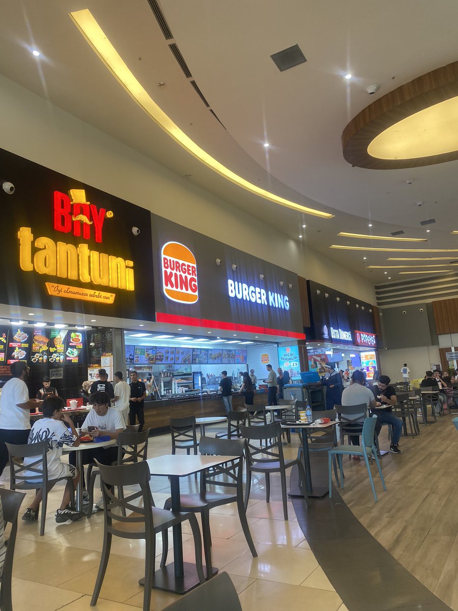timurince11's tweet photo. Bugün Malatya’da bir arkadaş ile PARK AVM’de randevulaştık. Üst kat yemek bölümünde beklemeye başladım. Yaklaşık yarım saat kadar…

Genelde hamburgercilerin olduğu alanda ilk gözüme takılan; yemek alan gençler henüz masaya oturmadan daha yürürken ilk başta aldıklarının fotoğrafını çekmeleri çok tuhafıma gitti. 

Genellikle genç kesimin uğradığı AVM’de şöyle bir göz gezdirdim. Gördüğüm kişileri incelerken; bakımlı, saçları, giysileri, ayakkabıları, çantalarına kadar her şey marka ve kaliteli. Ellerinde ki telefonlar en son çıkan modellerden. 

Şişmanlamış kızlar, derisi yere düşüp dökülecek oranda nazik ciltleri, çoğu makyajlı, hiç güneş görmemiş delikanlıları görünce cumhuriyet döneminde çıplak ayaklarla, oraklarla, nacaklarla Yunanlı Haci Anesti ordusuna karşı savaşan o dönemin yağız delikanlıla ile kıyasladım. 

Belliki hiç biri zoru görmemiş, ekmek kazanmak lügatlarında yok, çalışmamış, merdiven dahi çıkmamış, babası-annesi vermiş eline bol limitli bir kredi kartını çocuğumun her isteği yerine gelsin de ne olursa olsun konusunda taviz verilmeyen bir nesil var elimizde. 

Düşündüm de umarım bunlarla bir savaşa girmeyiz dedim içimden. Mg3’e şeriti takıp sıçrama yaparak düşmanım kalbine ateş edebilecek birinin olamayacağına kati suretle karar verdim. 

Sakarya da İngilizler tarafından donatılmış 100 bin kişilik Yunan ordusunu 3000 kişilik çıplak ayaklı, orak, nacaklarla durduran nesilden marka kotlu, göbeği prinçekli, gözlüksüz gezmeyen, hamburgerci nesile geldik.  

Maalesef her şeyi tükettiğimiz gibi gençleri de en basitleşmiş seviyeye indirgedik. Eğitemedik onları. Hamburger yemeden önce fotoğrafını çekmekten mutlu olmak harici hiç bir hacmi bulunmayan nesil önümüzde ki çeyrek asırda sanırım imtihanımız olacak.  

Günün sonunda en çok üzüldüğüm şey ise temizlik elemanları oldu. Orta yaşlarda 3 bayan belliki patronlardan azar işitmemek için gözleri masaları radar gibi gözetliyordu. Durmadan bir masadan diğer masaya. Ha bir de her yiyecek sonrası çıkan kaba çöplerde meğer bu hamburgercilerin göz boyama tekniğiymiş. Onu fark ettim. Yemek yerine bir sürü kâğıt, plastik alıyorsun.  Olan bitene sadece hayıflandım ve içerlendim.  Bu nesille hiç bir şey olmaz.  

Son dip not: iyiki köyde yaşıyorum.