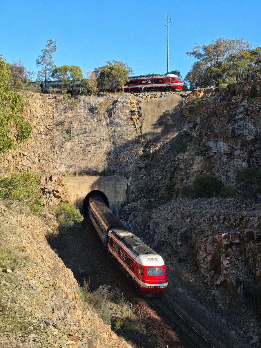AunzRailfan's tweet photo. メルボルンXPT最大の見所とも言えるループ線、Bethungra Spiralを前日とは逆の位置から撮影。どんなループ線かわかるよう撮影画像��ChatGPTで即席合成。
今回のXPTはメルボルン側機関車のみキャンディ復刻塗装。トンネルを通り、山を一周して上り線路が交差する様をより一層目立たせてくれました。 https://t.co/GC4XiYFZ2s