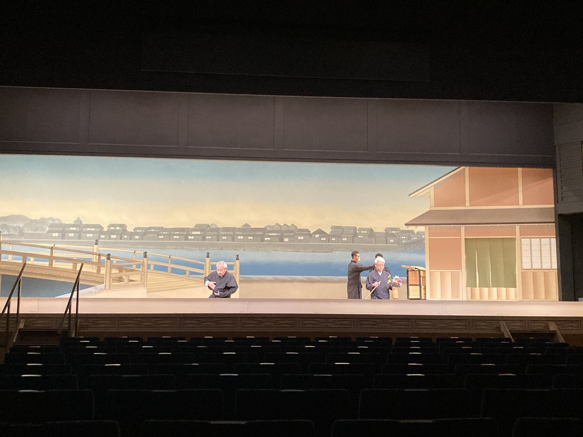 ono_hiroyuki's tweet photo. 【文楽『#まちの灯』振り返り６】
7月12日
この日は人形遣いの皆さんの稽古。前回の「場当たり」が全体のイメージをつかむシミュレーションだったとすれば、今日は実際に浄瑠璃の録音をかけながら最初から最後まで動きます。といっても、この日も主遣いの師匠方のみがいらっしゃって人形も持ちません。劇場の２階ロビーで、録音に合わせて演技をします。師匠方が人形になって動くのです。それにしても、人形がお上手な方は芝居がお上手。ご本人の芝居心・技術が、人形に伝わって増幅するのですね。
ほとんどの場面は師匠方が考えてこられた動きを１回あわせて確認。立ち位置の整理が必要な部分だけ、何度か返し稽古をしました。普段の古典の公演ではこのようなお稽古はありません。ツメ人形の皆さんに場面の気持ちをお伝えして立ち位置を決めたりしたのですが、それもこれまであまりなかったことだったらしいです。
懸案はラストシーンです。どう動くべきかについて勘十郎師・勘彌師と議論。あの奇蹟のクロースアップに込められたさまざまな意味と感情をどのように形にしたいかをお話しいたしました。映画だと一つのクロースアップで全てを表現するのですが、そこに奔流するあらゆる感情を分解分析して、人形の振り・表情の一つ一つ、浄瑠璃、三味線、照明、美術など総動員で文楽のラストシーンとして構築しなければなりません。難関です。
師匠方が事前に周到に準備してきてくださいましたのでスムーズに進みましたが、それでもこの日の稽古は合計６時間かかりました。

7月13日
この日は「道具調べ」。美術・大道具の確認です。新作文楽のために美術家が工夫を凝らした新しい美術に感動。１場面ずつ確認していきます。大仏は図面よりも少しかみてに変更するようお願い。幕を上げるタイミングや群衆の道具がガヤガヤする順番も決定。勘十郎師と蓑二郎師は川の杭の位置を決めて、大道具さんがその場で作ります。実際に技芸員が歩いてみて、「ここに平台が一段欲しいわ」となればテキパキと大道具さんが作業をします。大道具だけで��く、花籠を置く台の位置、花の色や本数などをどんどん決めていきます。小道具さんは花びらが落ちる仕掛けを作ってきてくれました。
私も神聖な国立文楽劇場の舞台にはじめてあがらせていただき緊張しました。（さすがに記念写真を撮ることは憚られました）

7月14日
この日のお稽古は、「立稽古」。「たて稽古」と読みます。舞台をやってる人なら、「実際に動いてみる、立ち稽古かな」と思ってしまいますが、文楽の世界では太夫と三味線のリハのことと言います。あくまで太夫と三味線の皆さんの通し稽古なので、舞台には幕をつり、人形遣いの皆さんは幕の後ろで音を聞きながら動いてみるか、楽屋に聴こえてくる音を聴いてシミュレーション稽古をするそうです。この日のリハは録音し、明日の稽古で使います。
改めて通して聞きましたが、素晴らしすぎます。字幕を出す人も一緒にお稽古です。
この時点でラストシーンの演出候補は「引き幕」か���緞帳」で終わるか、「ラストの三味線の長さをどうするか」など４パターンの候補があり、その分も録音しました。

7月15日
この日の稽古は「居処調べ」。前日の立稽古で録音した義太夫を流しながら、実際の舞台美術の中で人形遣いが演技をします。
吉矢さんから稽古冒頭に何か一言話しますか？と言われ、一言ご挨拶というのもおこがましいように感じましたが、改めて決意を述べさせていただこうと思い、「ユージーン・チャップリンさんから先ほど飛行機に乗ったという連絡をいただきました。とても楽しみにしておられます。歴史的な舞台、どうか成功しますようお願いします！」と申し上げました。その時、技芸員さんから拍手が起きて感激。この道数十年の師匠方がこれまでの経験と芸、何よりすごい情熱を込めて全身全霊で新作に取り組んでおられる。みんなが成功に向けて一丸となっているのを感じて、稽古が始まりました。
さてこの日もまだ人形は持ちません（正確には大仏のシーンだけ勘十郎師は人形をお持ちになり、確認なさっていました）。主遣いが実際に動きながら確認・修正。左と足遣いの皆さんは舞台脇に��ばりついて主遣いがどう動くかを見て、ご自分の動きを研究なさっています。いよいよ形になってきました。相撲シーンは爆笑もの。玉助さんのご提案で大文字屋のセットのしもてにあった格子を、お客様��ら座敷の中がよく見えるように、その場で外してもらいました。
前日まで４パターンの中で迷っていたラストは引き幕に決定し、照明のタイミング、幕を引くタイミングもばっちり決まりました！
#新作 #文楽 #チャップリン #国立文楽劇場 #街の灯

写真は道具調べ、立稽古、居処調べの様子。