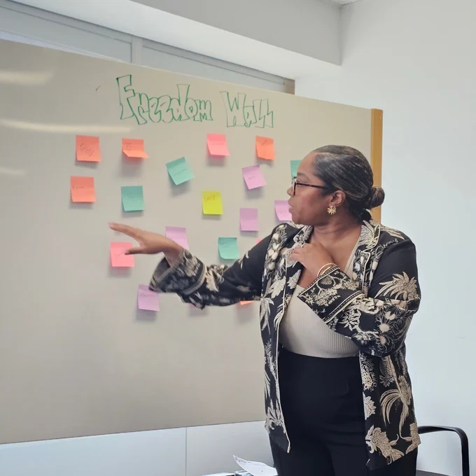 Woman pointing at colorful sticky notes on a whiteboard titled 'Freedom Wall' during a discussion.
