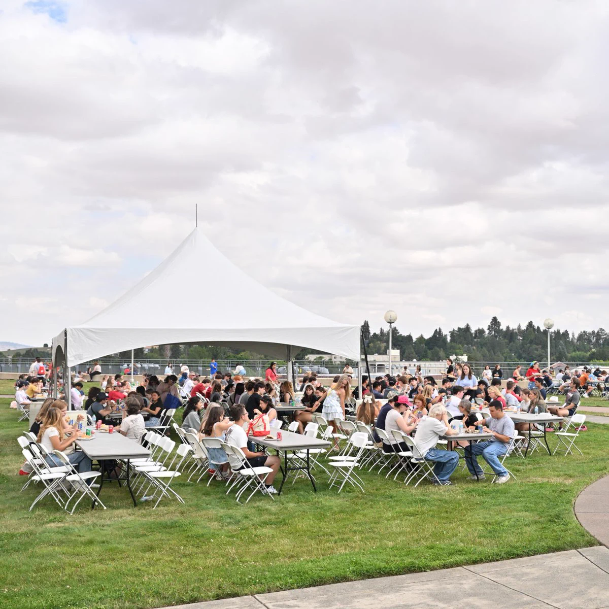 Color outdoor photo of people eating at tables during a picnic. 