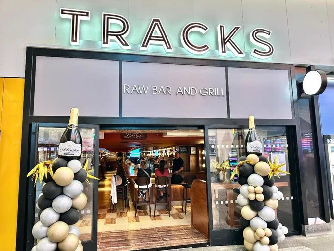 The exterior of TRACKS Raw Bar and Grill at the LIRR Concourse at Penn Station, with black, white, and gold balloons decorating the entrance.