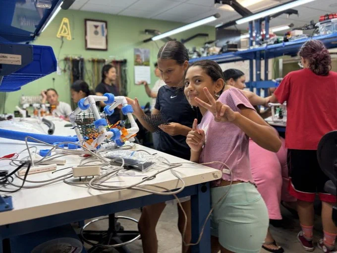 Two students build a SeaPerch II ROV in a makerspace workshop while one shows the peace sign.
