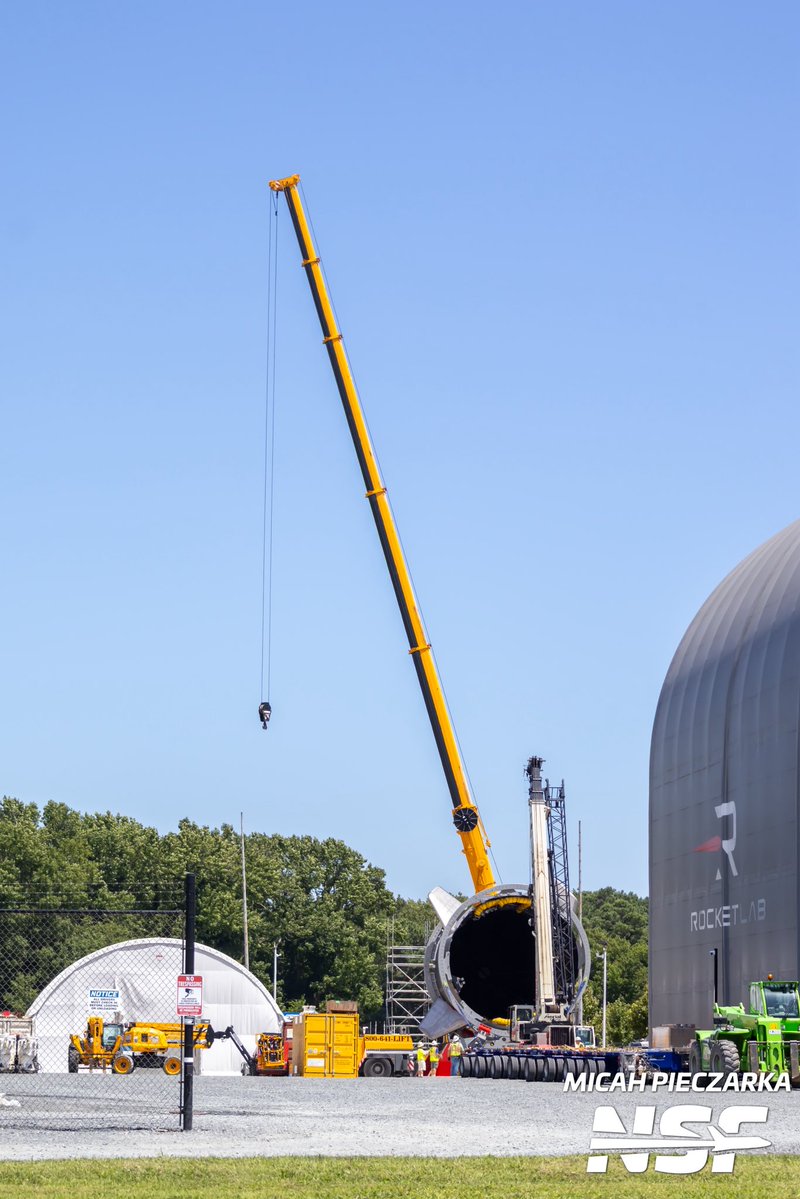 EShoreSpaceflt's tweet photo. Rocket Lab Neutron AIC update

The Hungry Hippo fairing is out for some fresh air. It has been moved to the back of the AIC, right where the old Stage 2 static fire test stand used to sit. Looks like they got it out of the Building 01 integration building and backed it over there without much trouble, using that trailer moving equipment spotted a few nights ago.

Right now it is sitting on red support stands on the blue transport trailer, waiting for its lift. Based on the setup, it looks like they are getting ready to stand the fairing up vertical, which would line up with the speculation from a few days ago. 

@NASASpaceflight