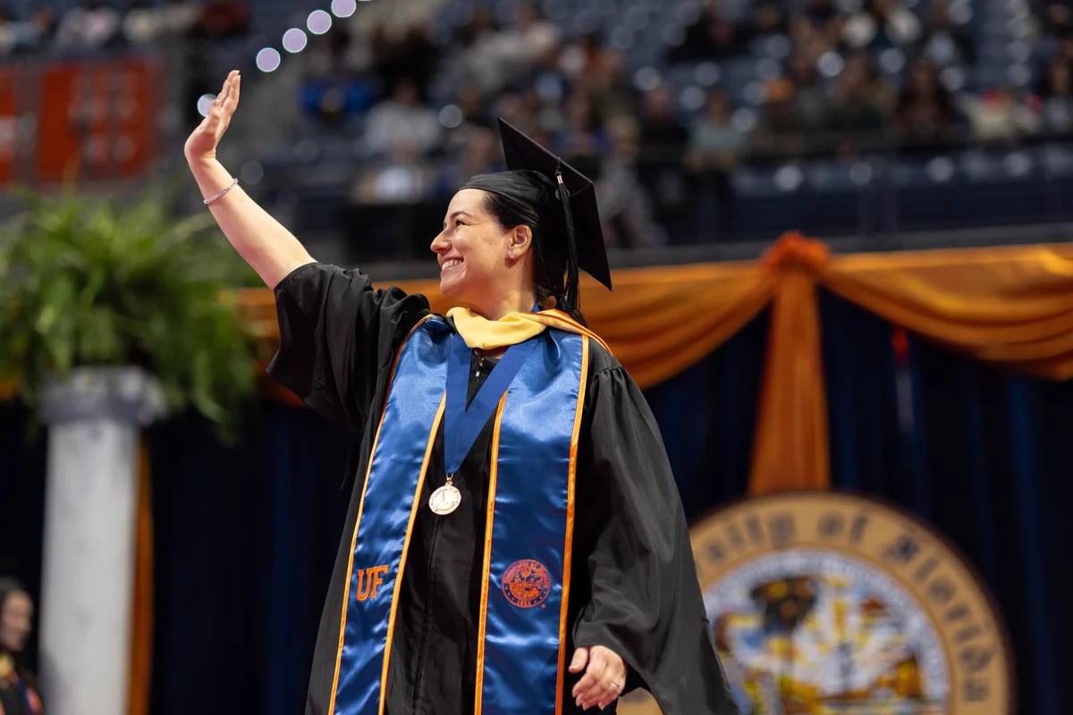 Student wearing a graduation robe walking the stage and waving to the crowd