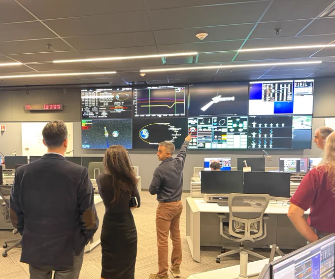 A man standing pointing to a wall of large screens with detailed images and data from space.