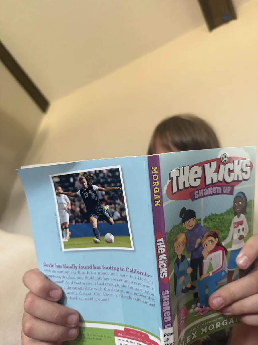 Young girl buried behind a book about a girls’ soccer team