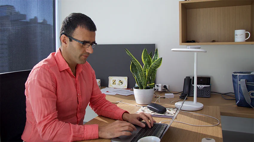A man wearing glasses works at a computer inside a modern office. 