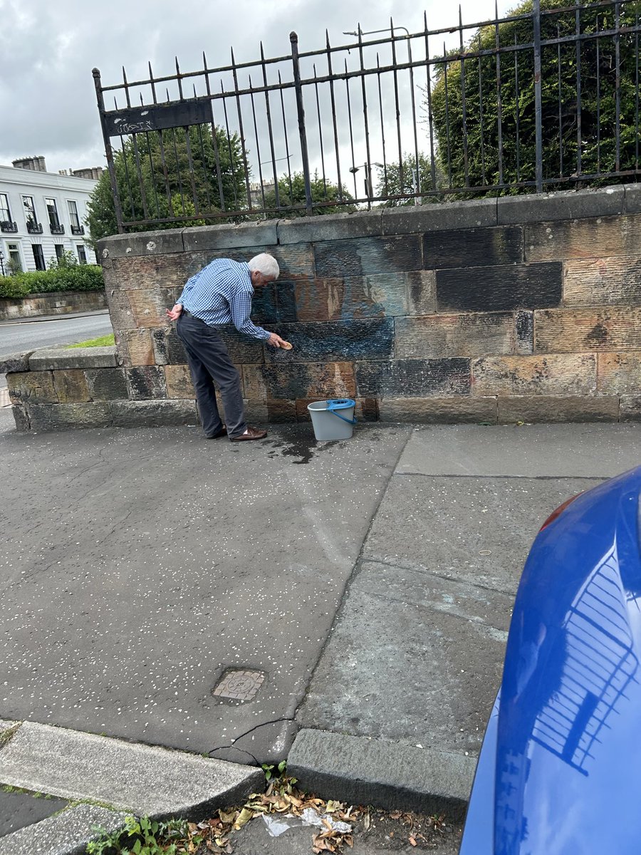 Annemarieward's tweet photo. I drove past this gentleman in Glasgow today, got about thirty seconds down the road, then turned the car round.

I wanted to thank him.

Bucket of water. Scrubbing brush. Quietly removing graffiti from an old sandstone wall. Nobody paying him. No council van. No strategy, task force or community empowerment initiative. He’d simply seen something being spoiled and decided to do something about it.

Just around the corner is the Mitchell Library.

Someone has sprayed a huge black tag across the sandstone of one of Glasgow’s great civic buildings.

Glasgow is becoming saturated with this stuff. There has been speculation that some of the newer tagging is connected to drug gangs and changes in the illicit drugs market. I don’t know whether that’s true, and speculation isn’t fact. But we don’t need to know who’s doing it to see what’s happening to our city.

And I refuse to accept that caring about this is somehow petty.

The Mitchell wasn’t built simply to store books. Previous generations built places like this with beauty and grandeur because they believed ordinary Glaswegians, knowledge and civic life were worth something.

We inherited their city.

For a little while, it’s ours to look after.

That’s what struck me about the man with the bucket. He wasn’t cleaning his property. He was cleaning our wall.

You can’t manufacture that through government policy. It comes from something much older and more important: the belief that where you live belongs to you in some small way, and therefore you owe something back to it.

Within a few hundred yards today I saw two attitudes towards Glasgow.

One says: I can do what I like to this place.

The other says: This is our place. I’ll look after it.

I know which one builds a city.

And I know which one destroys it