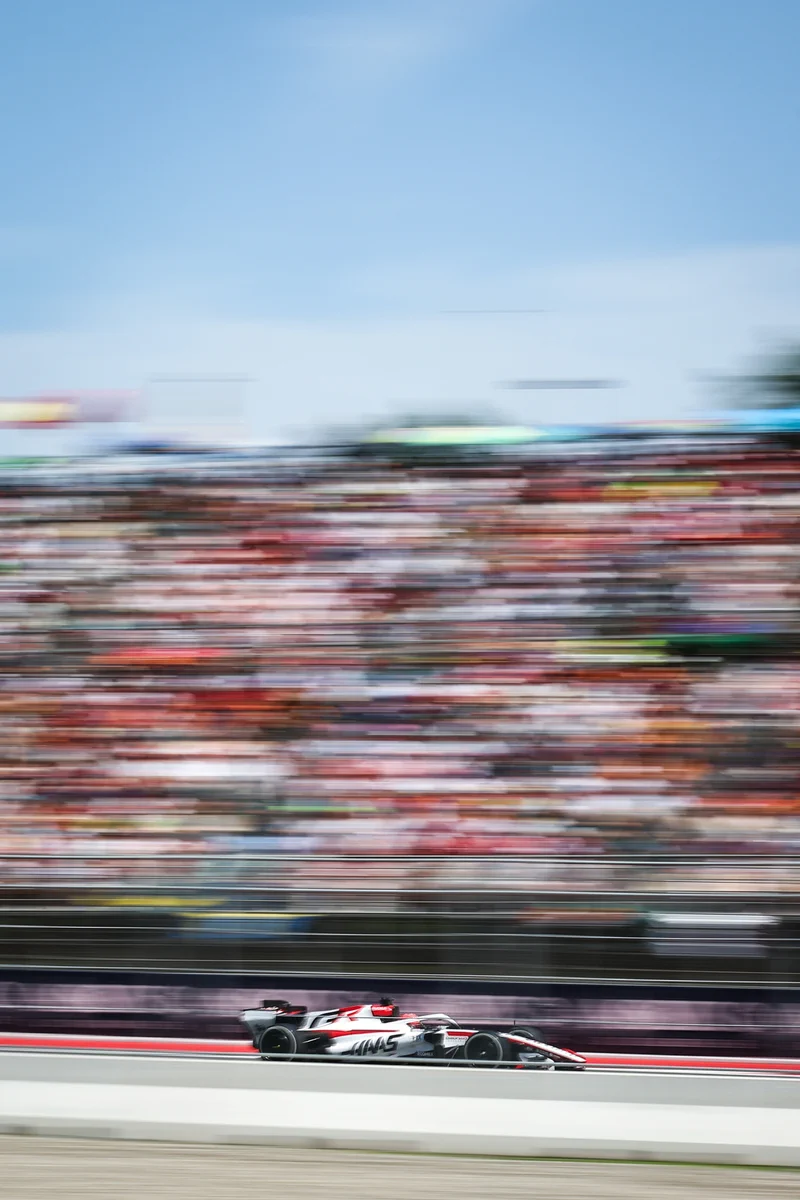 A Formula 1 race car is speeding on a track with blurred grandstands full of spectators in the background under a clear sky.