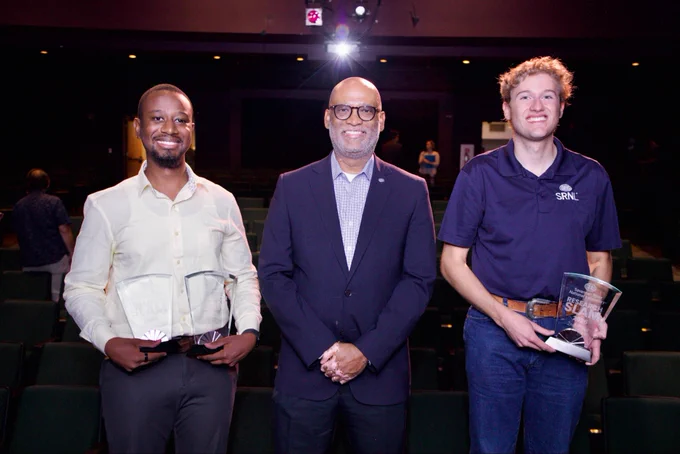 Two winners on stage with awards with lab director Johney Green