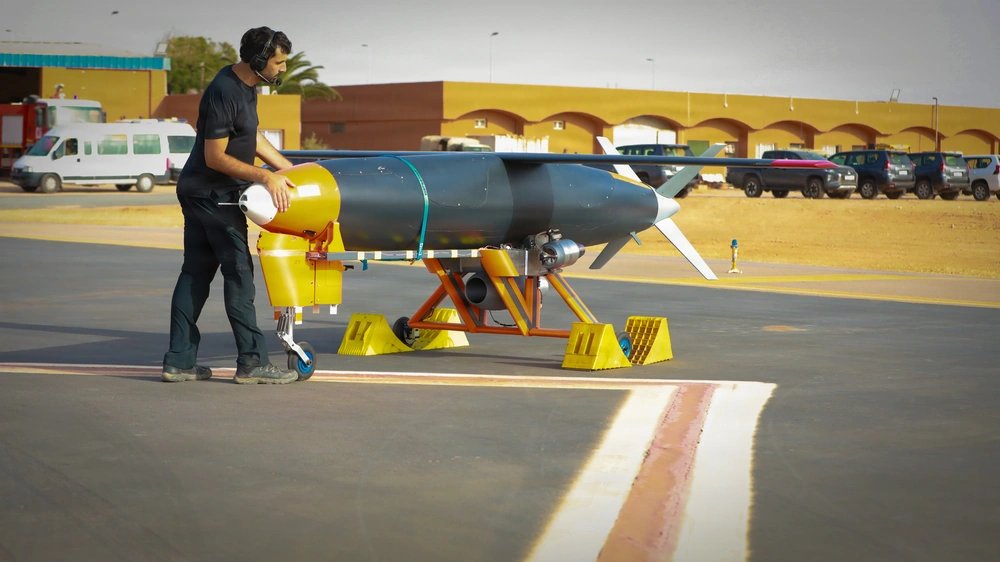 MoroccoIntel's tweet photo. 🇲🇦🇺🇸#FLASH| La toute première démonstration de tir réel dans le nouveau centre d'expérimentation technologique militaire AMTEC 🇲🇦🇺🇸 à Tan-Tan, a permis de tester avec succès le missile Anthem, un système de missile de croisière low-cost à longue portée développé par l’entreprise privée californienne Covenant Industries 🇺🇸.
L’AMTEC, Africa Multidomain Training and Experimentation Center, est un important centre africain d’entraînement, d’expérimentation et d’innovation militaires, développé conjointement entre le Maroc 🇲🇦 et les États-Unis 🇺🇸 par le bias de l'Africom à Tan-Tan.
Cette démonstration intervient alors qu'Anthem 🇺🇸 prépare ses équipements en vue d’une entrée en production sur sa chaîne de fabrication dès le début de 2027.
Le développement d’Anthem répond notamment à plusieurs besoins capacitaires mis en évidence par les conflits récents, dont la guerre en Iran 🇮🇷, et illustre la volonté d’AFRICOM et du Maroc de réduire considérablement les délais entre l’innovation technologique, l’expérimentation sur le terrain et la mise à disposition de capacités opérationnelles pour les combattants.
Actuellement, certaines entreprises doivent attendre 12 à 18 mois avant d’obtenir un créneau sur des infrastructures d’essais américains 🇺🇸 comme le champ de tir de missiles de White Sands.
Le secrétaire à l’Armée de terre, Dan Driscoll, a indiqué que l’objectif de l’armée américaine était de ramener ce délai à 30 jours.
Cette accélération repose notamment sur la mise à disposition de nouveaux espaces d’expérimentation, dont l’AMTEC au Maroc 🇲🇦.
Le 13 juillet 2026, les Forces Armées Royales ��🇦 marocaines et l'AFRICOM 🇺🇸 avaient signé, au quartier général d’AFRICOM, un protocole d’accord visant à établir l’Africa Multidomain Training and Experimentation Center.
À l’horizon 2030, l’AMTEC 🇲🇦🇺🇸 devrait s’articuler autour de trois composantes principales implantées à Tan-Tan :
- une zone de formation multidomaine
- une académie spécialisée dans les drones
- un centre d’innovation et d’expérimentation
Le complexe de tir et d’expérimentation multidomaine (MDTA) offrira ainsi un espace physique dédié permettant de tester les forces, les équipements et les nouveaux systèmes dans des conditions réalistes, afin de garantir leur aptitude à opérer efficacement dans différents environnements.
L’une des caractéristiques majeures du MDTA 🇲🇦🇺🇸 sera sa capacité à fonctionner sur l’ensemble du spectre électromagnétique, y compris dans des environnements électromagnétiquement contestés.
À terme, l’AMTEC 🇲🇦��🇸 pourrait donc devenir une plateforme stratégique reliant directement innovation, expérimentation, entraînement et déploiement opérationnel, tout en permettant aux États-Unis et au Maroc d’accélérer le développement et la validation de nouvelles technologies militaires sur le continent africain.