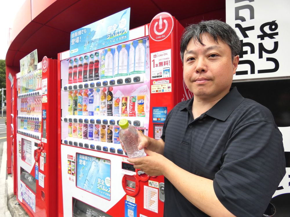 shokuhinet's tweet photo. コカ･コーラシステムは自販機にラベルレスボトルを初導入して新境地を開拓する。

　食品表示法や計量法などの法令･省令改正により、7月30日、ラベルレスボトルの自販機での販売が解禁されたことを受けた動き。

　従来の規制が緩和され、原材料名などの必要表示項目の文字サイズを従来よりも小さくでき、これにより表示項目の少ない水カテゴリの商品などではキャップに全ての表示項目を表記することが可能になった。

　8月3日、日本コカ･コーラが業界に先駆けて導入を発表し、自販機オペレーターの負荷軽減のため夏場の繁忙期を避けて10月からコカ・コーラシステムの自販機に「い・ろ・は・す 天然水 ラベルレス」を順次導入していく。
　現在、コカ・コーラシステムの総自販機台数（約75万台）の約95％に「い・ろ・は・す 天然水」が導入されている。

　この日、日本コカ･コーラ本社（東京都渋谷区）前の自販機でデモンストレーションした日本コカ･コーラの大島遊ベンディング事業本部ベンディングRGMXシニアマネジャーは「飲み終わった容器をリサイクルボックスに入れる際、ラベルを剥がす手間がなくなり、お客様の利便性向上とリサイクラーさまの負担軽減につながる。直接、消費者と接することのできる販売チャネルでサステナビリティが推進できる」と語る。

　「い・ろ・は・す 天然水」は2020年4月にラベルレスの発売を開始以降、これまで主にオンライン通販などを通じたケース販売を中心に展開。同社のラベルレスボトルは現在、9ブランド29品（SKU）をラインアップし、オンライン通販全体の売上の3～4割を占める。

　全国清涼飲料連合会の「清涼飲料水容器のリサイクルに関する消費者意識調査2025」（n=1037）によると、自宅でキャップとラベルの両方を剥がす人は 約80%に上る一方で、屋外では約30%にとどまり、屋内と屋外で分別の実施率に大きなギャップがあることが判明。

　今回の自販機でのラベルレスボトルの販売は、屋外でのリサイクルの促進に寄与しうる取り組みでもある。

　ラベル付き商品との誤認を防ぎ、ラベルレスであることを知らしめる取り組みとしては、視認性を高めたダミーのほか、トップボードやA3サイズのポスターを用意している。
　コカ・コーラ公式アプリ「Coke ON」の活用は「選択肢としてはあると思うが、まだ決まっていない」という。

　「い・ろ・は・す 天然水 ラベルレス」以外のラベルレスボトルの導入については「当社」としても非常に重要な取り組みであると位置づけており、もちろん可能性はある。まずは『い・ろ・は・す 天然水 ラベルレス』を販売してみてお客様の受容性や反応をみていく。展開できるものとそうでないものが恐らく出てくる」との見方を示す。

　キャップは、全ての表示項目を表記する必要性から、かすれたりしないように印字されている。 #い・ろ・は・す #飲料 #い・ろ・は・すみかん #ラベルレスボトル #コカ･コーラシステム #キャップ #ラベルレス商品 #日本コカ･コーラ #自販機 #ラベルレスペットボトル