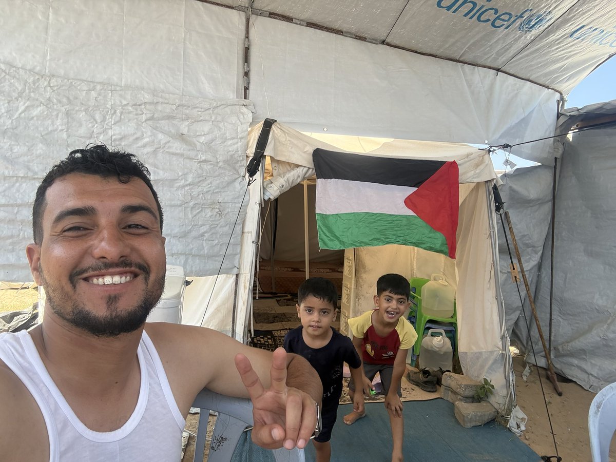 mohammedIhysse's tweet photo. Behind us is a tent… and above it flies the flag of our homeland. 🇵🇸

This is me with my two children, Imad and Adam, in Gaza.
We lost our home and so much of the life we once knew. This tent has become our home… but look at our faces: we are still smiling.

I want my children to grow up remembering that even the hardest days of their lives could not steal their hope.

We are still here. We are still alive. And we still dream of the day when we can leave this tent behind and live safely in a real home again. 💔🍉

From our tent in Gaza, we send you love and hope. 🇵🇸❤️