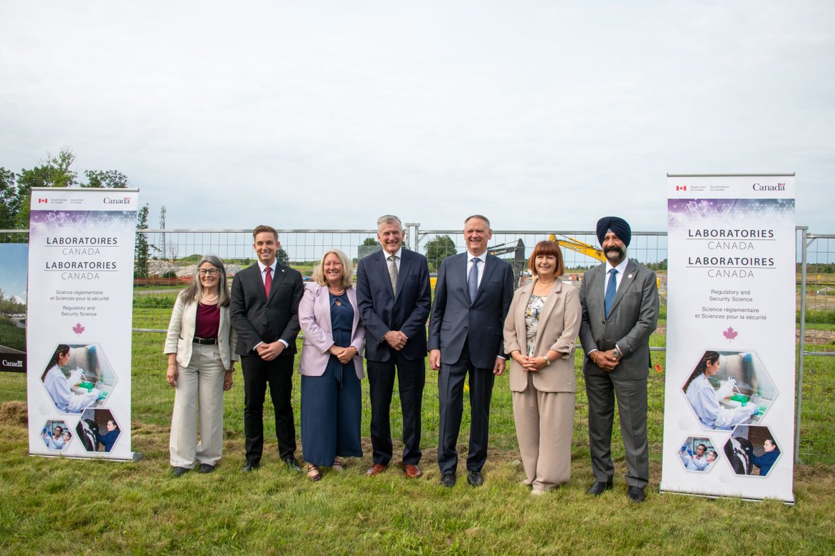 Group of seven diverse individuals posing on a grassy field with Canada Laboratories signs on each side.