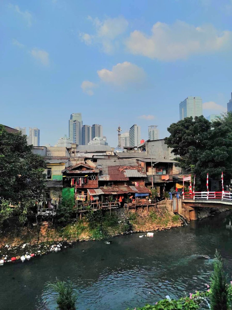 stravenues's tweet photo. Ada satu hal lagi juga yang agak mengganggu admin soal bagaimana pemerintah seharusnya memaknai perayaan kemerdekaan ini lebih dari sekadar seremoni dan pertunjukan di Istana.

Coba turun ke kampung-kampung, ga usah daerah 3T, di Jakarta aja. Foto kiri diambil awal bulan Agustus 2026, di bantaran Kali Krukut Bendungan Hilir. Cuma 1-2 km dari Sudirman dan daerah gedung pencakar langit.

Di sana, terlihat ada gapura nuansa merah putih dan juga umbul-umbul merah putih--sebuah semangat perayaan HUT RI di akar rumput yang jauh dari sentuhan pemerintah dan ingar bingar di Istana.

Sangat miris, sudah 81 tahun merdeka, permukiman kumuh di bantaran kali di pusat kota Jakarta masih ditemui. Kalau saya berbohong dan bilang foto ini diambil 10-20 tahun yang lalu, orang mungkin akan percaya--saking tidak ada progressnya. Sayangnya, alih-alih dipandang dengan kritis, orang cenderung meromantisasi ini dengan bumbu patriotisme.

Sementara itu, foto di kanan adalah cover dari postingan @/theindigenousnarrative di Instagram, soal bagaimana balkon-balkon HDB memasang Bendera Singapura dan logo National Day.

Foto di kanan terasa sangat dalam, karena bagaimana pemerintah mampu merumahkan sebagian besar rakyatnya dalam flat HDB, mentransformasikan gaya bermukimnya, dan menjadi sebuah milestone keberhasilan yang patut dirayakan dalam hari kemerdekaan.

Stagnansi yang terlihat dari bagaimana warga negara kita bermukim sangat bertentangan dengan tujuan berdirinya Republik Indonesia yang tercantum dalam pembukaan UUD 1945, tepatnya tujuan no 2 yaitu "memajukan kesejahteraan umum".

Pada akhirnya, negara memang terus menerus mempertahankan tradisi 17an yang dipersempit dalam bentuk lomba dan selebrasi, tanpa pernah melihat bahwa ini adalah sebuah masalah dan kegagalan negara memenuhi itu.