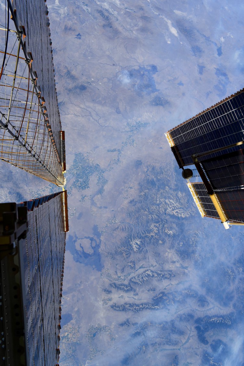 Astro_Jessica's tweet photo. While I wasn’t gazing at @astro_anil during last week’s spacewalk, my eyes were drawn downward to our majestic Mother Earth.  Here’s how she looked from my spacesuit.
Photo 1: Coastal view framed by the @Space_Station solar arrays.
Photo 2: The sun sets behind our newly installed IROSA mod kit, a mounting platform for new arrays to be installed on an upcoming spacewalk (like the shorter array in lower left of photo 1).
Photo 3: Mountain views framed by the @Space_Station  solar arrays.