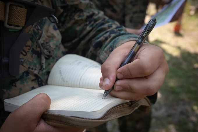 U.S. Marine records land navigation information during field training with multinational forces.