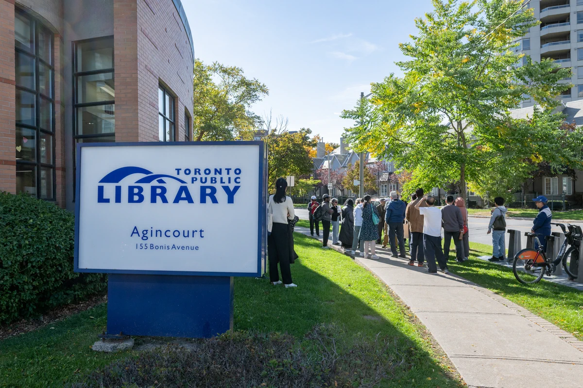People waiting in line outside the Toronto Public Library Agincourt branch on a sunny day.