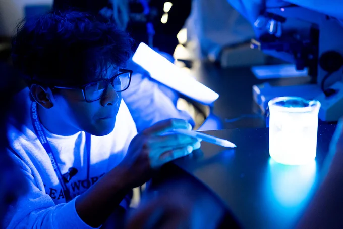 Student examines a glowing beaker amid blacklight.