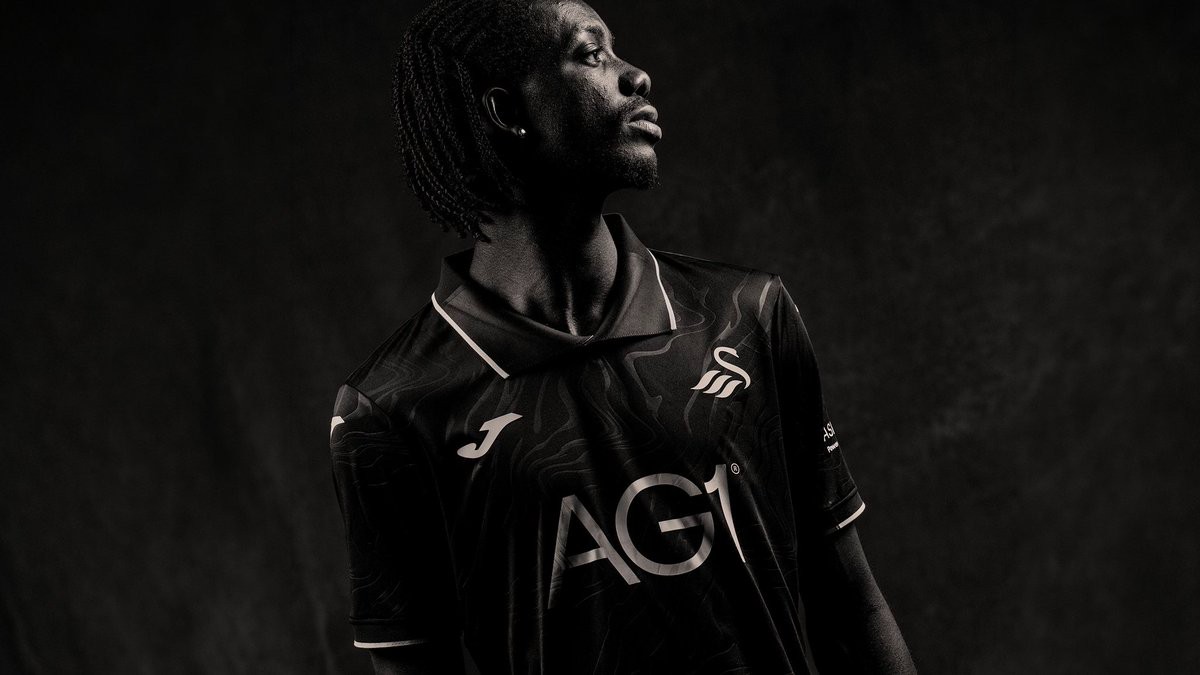 Footy_Headlines's tweet photo. 𝙎𝙬𝙖𝙣𝙨𝙚𝙖 𝘾𝙞𝙩𝙮 𝟐𝟔-𝟐𝟕 𝙏𝙝𝙞𝙧𝙙 𝙆𝙞𝙩 𝙍𝙚𝙡𝙚𝙖𝙨𝙚𝙙

Swansea City and Joma have officially launched the club's new third kit for the 26-27 Championship season. The new strip completes the Swans' kit collection for the campaign, offering a sleek look inspired by the local coastline.

The Joma Swansea City 26-27 third shirt features a black base overlaid with a subtle tonal wave pattern across the body. A classic polo collar and matching sleeve cuffs feature crisp white piping, complemented by silver-white detailing for the Joma logo, principal sponsor AG1, and the standalone swan crest.

As with the home and away jerseys, Welsh identity is embedded throughout the shirt, with "ABERTAWE" printed on the upper back neck and the club slogan "Ein Hanes. Ein Dyfodol. Ein Ffordd." featured inside the collar label. Black shorts and socks complete the new Swansea City 26-27 third kit.