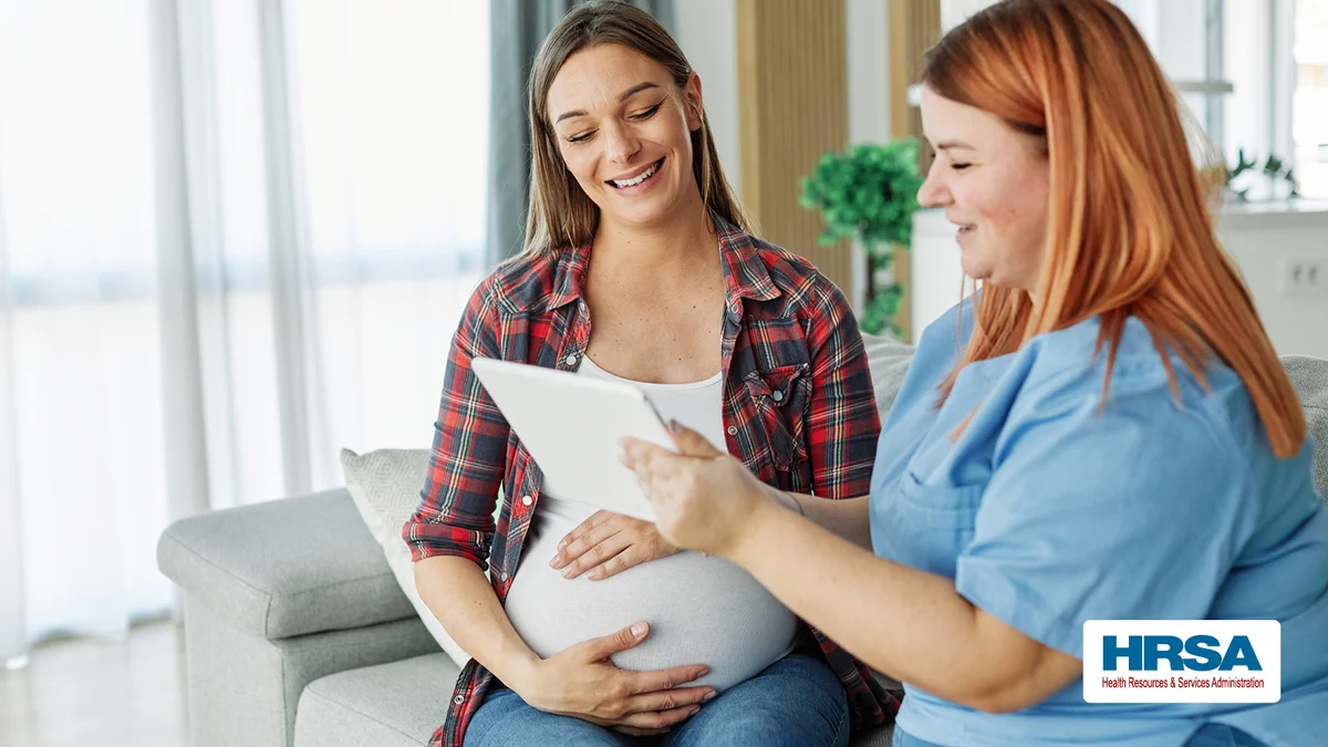 A home visitor sitting with a pregnant woman going over information on a tablet.