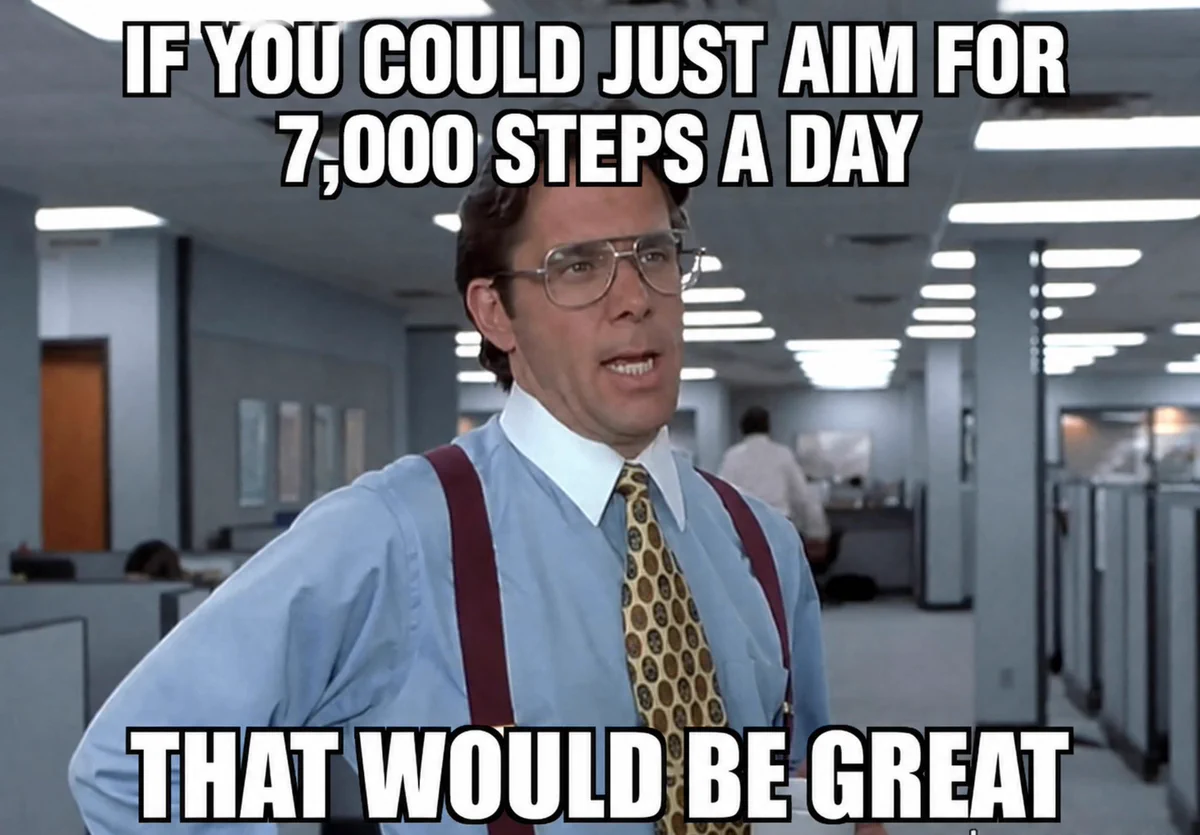 A man in a business suit speaks in an office setting, emphasizing the importance of aiming for 7,000 steps a day for health.