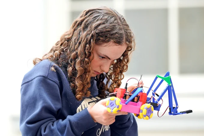 A student tinkers on a colorful robot with wheels. 
