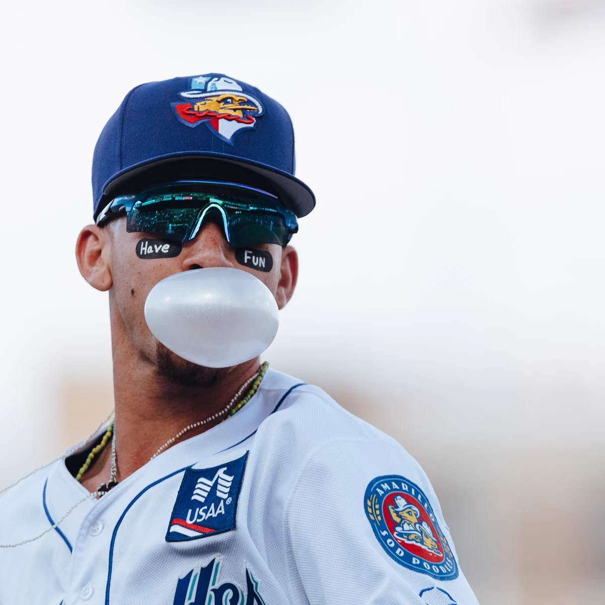 Baseball player blowing a bubble with eye black reading “Have Fun.”