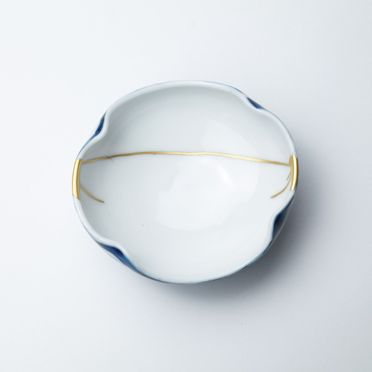 tsugu_kintsugi's tweet photo. 内側は白磁、裏��に千客万来や魔よけの意を持つ八つ手の染付の入った向付。両端に大きなカケヒビ、２分割を滑らかに結ぶ金線で継がれています。 https://t.co/VT133mThMz
