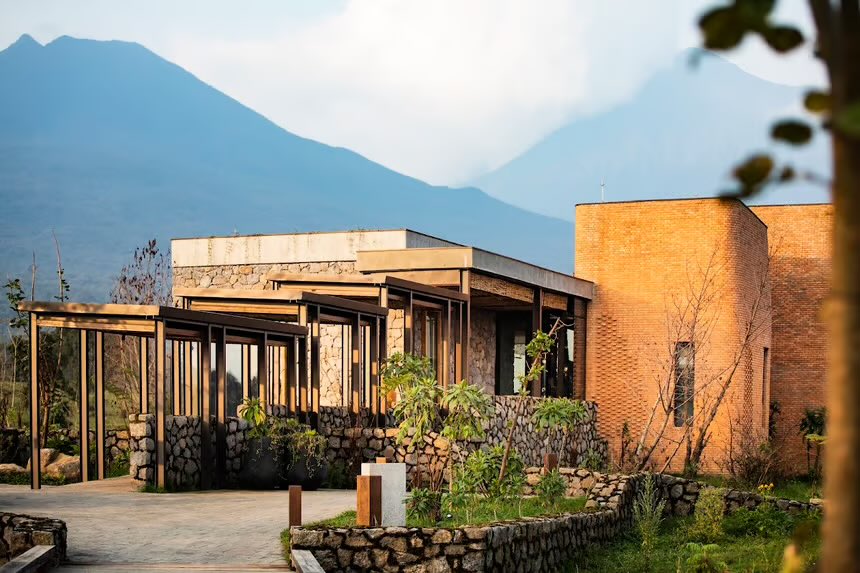 shavnyuyngah's tweet photo. This is a villa built because 320 endangered mountain gorillas live ten minutes away.

Kataza House sits in the shadow of the Virunga volcanoes, named after a silverback gorilla, and everything about it is in dialogue with Volcanoes National Park. Mountain bamboo and forest trees surround the structure. Clay brick and volcanic stone sit as two distinct volumes, hand-fired by nearby communities, warm against the cold precision of stacked river rock. It doesn’t sit on the landscape, it’s mid-conversation with it, tall dry grass in the foreground, mountain on the horizon, everything lit gold in late afternoon light.

Look closer and nothing here was sourced from a catalog. Volcanic rock pulled straight from the site. Woven bamboo ceilings built in place, not shipped in. Sculptural wooden furniture and a fireplace carved into raw stone, the kind of interior that looks collected over decades, not designed in a season. The palette doesn’t decorate around the landscape, it repeats it, clay reds, charred blacks, the exact colors of the volcanic earth outside the window.

That undulating woven light installation, the one that looks like it’s rippling mid-motion, is Kenyan artist Were Osewe’s work, and it does what the whole house does in miniature: takes a material everyone assumes they already understand and asks it to move differently.

This is proof that luxury and place don’t have to be opposites. Rwanda didn’t import an aesthetic to build something world-class. It built with what surrounded it, and let that carry the weight.

Volcanoes National Park region, Rwanda · Photography: Kataza House