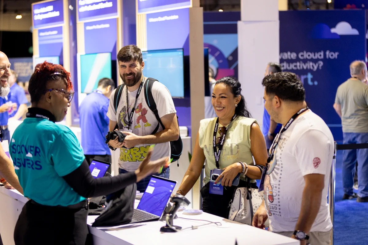 A group of four people stands at an information booth during VMware Explore. One person behind the counter is wearing a "Discover Answers" shirt.