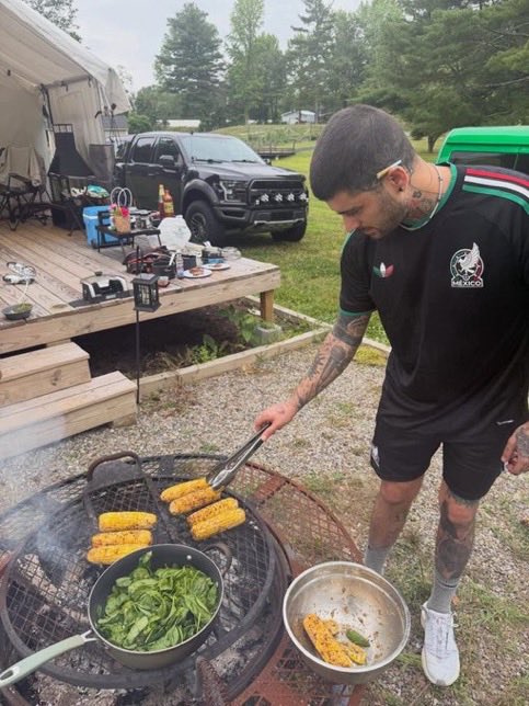 Indie5051's tweet photo. Zayn con una playera de México, asando elotes y con una salsa valentina en el fondo. https://t.co/pKLJM8yuoI