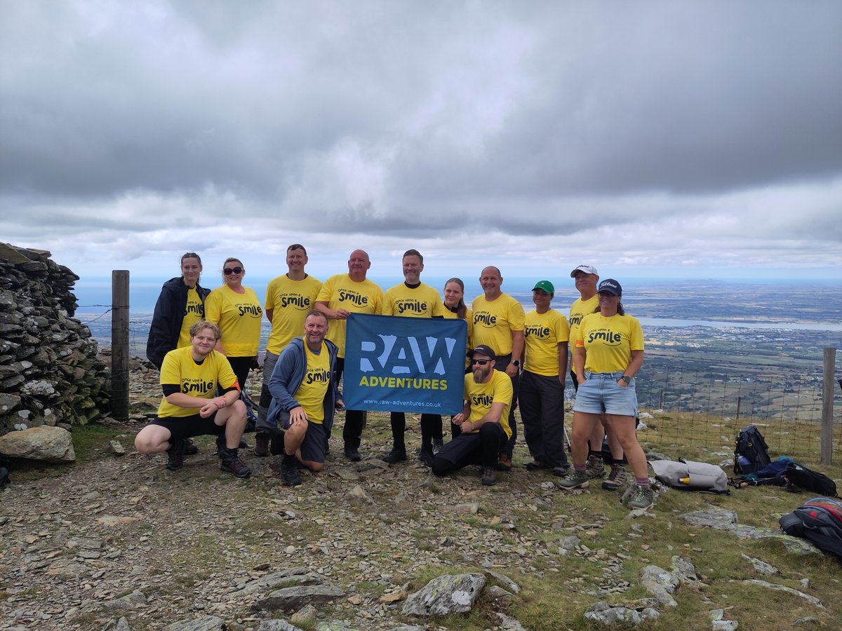A group of people at the top of a mountain wearing yellow t-shirts with the charity logo on
