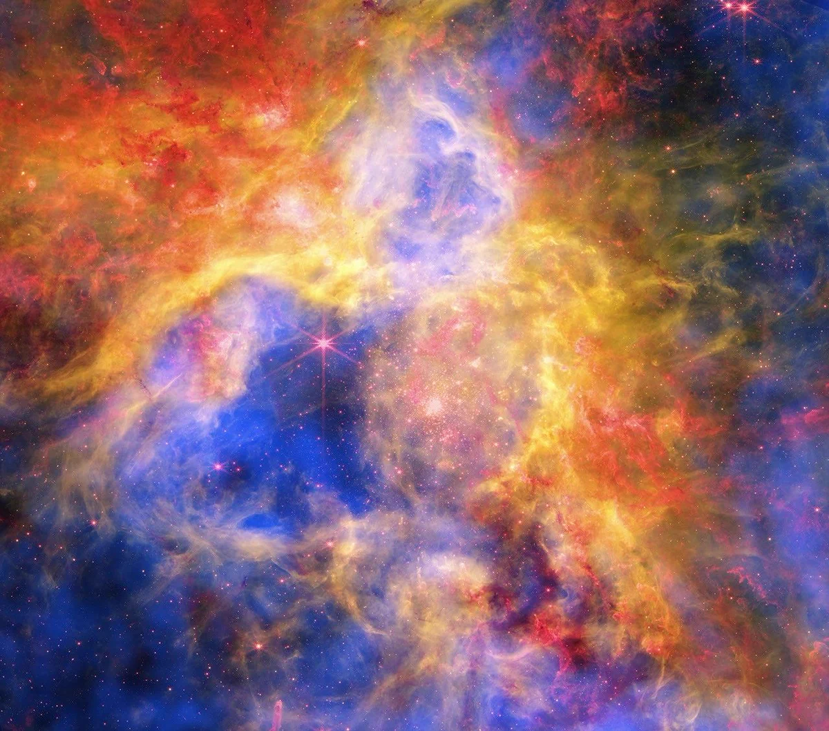 The Tarantula Nebula—vibrant and colorful. Clouds of red, yellow, orange, and green crest over a background of deep blue haze, black space, and red stars. Bright spots of light line the center, causing parts of the clouds to glow luminous gold. Credit: X-ray: NASA/CXC/Ohio State Univ./J. Rodriguez et al; Infrared: NASA/ESA/CSA/STScI; Optical: NASA/ESA/STScI; Image Processing: NASA/CXC/SAO/P. Edmonds