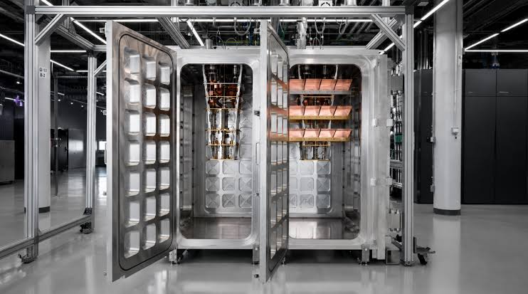 Qtumanalysis's tweet photo. Remember the wiring wall?

IBM just took its shot at it.

Yesterday they connected two cryo chambers into one ultra cold environment. First time at this scale.

A quick recap: superconducting qubits need cables into a fridge. Fridges run out of room and the biggest chip ever, 1,121 qubits, hit that ceiling. IBM never built a bigger one.

So they stopped making bigger fridges. The new design scales by adding modules.

Box shaped cells that connect in a row. Each one 12x the wiring space, ~2,000 qubits. Two cells just cooled to 15 millikelvin as one system. The key piece is L-couplers, Meter long superconducting cables carrying quantum information between chips in different modules.

And the detail most missed, those cables attack superconducting's OTHER weakness too. Long range connections unlock error correction codes with ~10x less overhead.

One cable fixing Two problems, If it works.

Because yesterday's chambers were empty. No qubits inside. On chip couplers entangle across micrometers. These cables must do it across a meter. A million times farther.

The real test is late this year, IBM puts live chips in both boxes and runs operations across the boundary. If fidelity holds, the two biggest arguments against superconducting weaken in one experiment.

If not, the scaling story has a meter long hole in it. Empty boxes today. The most important test in quantum in months.

$IBM $INFQ $IONQ
