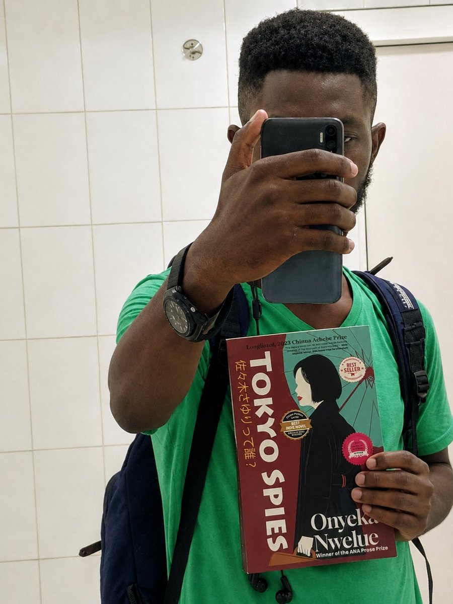 IZRLTRCZ's tweet photo. Me,
With the book    vs.    The Book.

“Tokyo Spies” by @onyekanwelue 

This one na interesting story wey blend art, love, family, and the struggle wey person fit face when life put am for difficult position. Zenjiro Ito’s journey from Japan to China make the story dey feel like journey of fear, escape, and self-discovery. Wetin I like pass na how Nwelue show human weakness without making the character look completely hopeless. The writing get quiet, reflective moments, but e still carry suspense. Some parts fit move slowly, but overall, na thoughtful book wey dey make you think about courage, identity, betrayal, and the choices we make when we dey afraid.
#OizamsiReads