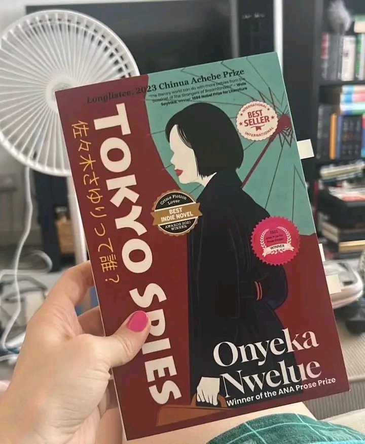 IZRLTRCZ's tweet photo. Me,
With the book    vs.    The Book.

“Tokyo Spies” by @onyekanwelue 

This one na interesting story wey blend art, love, family, and the struggle wey person fit face when life put am for difficult position. Zenjiro Ito’s journey from Japan to China make the story dey feel like journey of fear, escape, and self-discovery. Wetin I like pass na how Nwelue show human weakness without making the character look completely hopeless. The writing get quiet, reflective moments, but e still carry suspense. Some parts fit move slowly, but overall, na thoughtful book wey dey make you think about courage, identity, betrayal, and the choices we make when we dey afraid.
#OizamsiReads