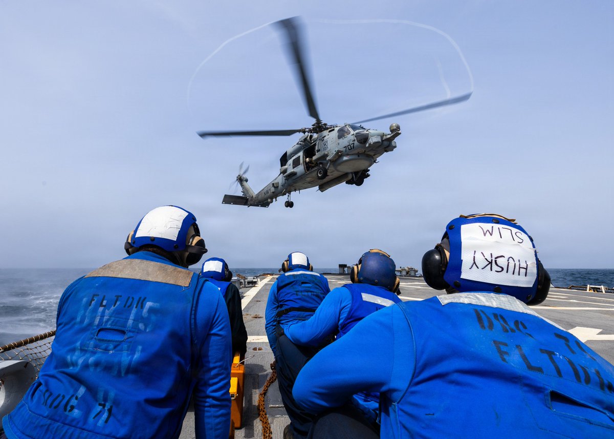 Sailors aboard the Arleigh Burke-class guided-missile destroyer USS Ross (DDG-71) observe an MH-60R Seahawk landing on the ship's flight deck while operating in support of the U…