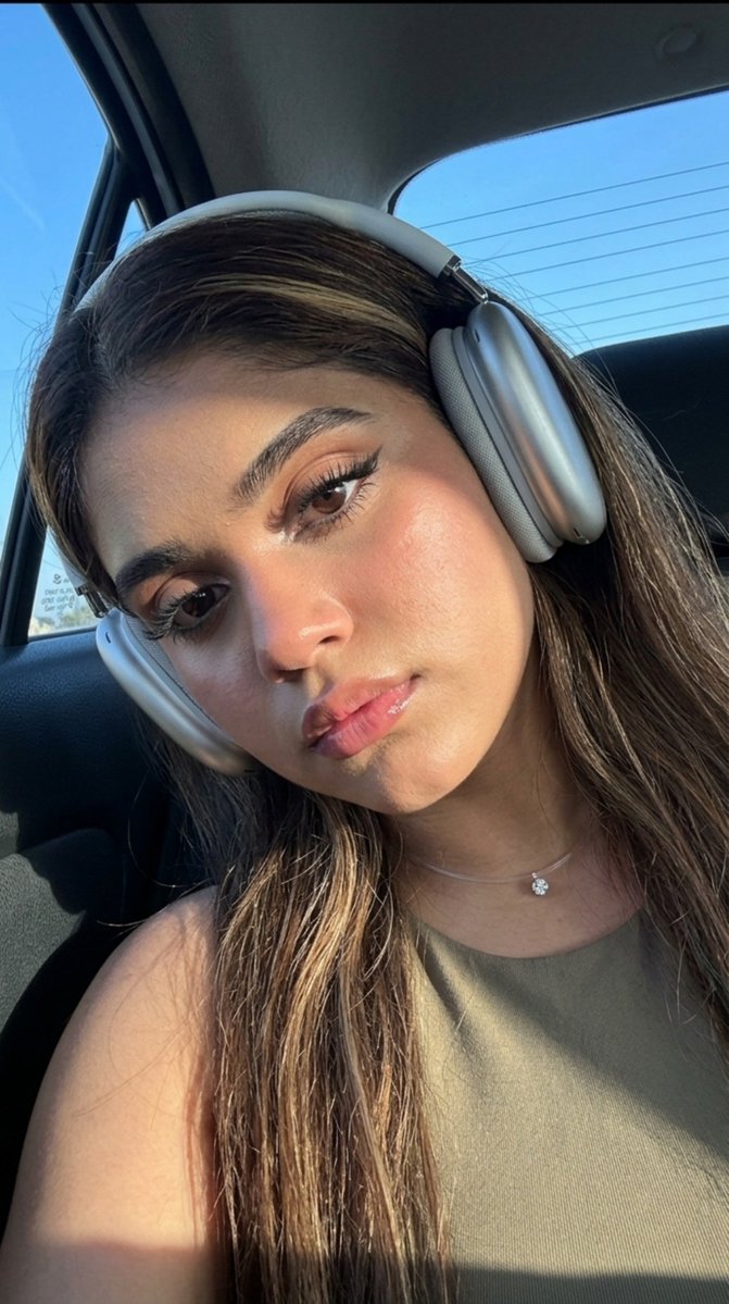 oye_samia's tweet photo. Off-duty aesthetic. 🎧 

Prompt: Without changing the appearance of the girl in the photo, do not change the color of her eyes. Selfie on the front camera, super close-up. The angle from below (low angle). The girl has thick long hair that falls over her shoulders and back. Glowing skin. Makeup: neatly designed dark eyebrows with lamination effect, extended eyelashes in a "fox" effect, highlighter in the corners of the eyes, long black arrows, glossy lips. He wears large silver headphones on his head. She's wearing a khaki tank top. There is a thin transparent fishing line with a small diamond around her neck. Calm facial expressions, head slightly tilted to the side, confident seductive gaze down into the camera. She's sitting in the back seat of the car by the window. The blue sky is visible through the rear and left side windows of the car. The girl is slightly lowered down on the seat, because of this, her face is in shadow. Lighting: bright natural light falling from the side, from the back, beautiful clear shadows on the shoulder, light highlights in the hair. promsmy. Photorealism, high detail. The photo was taken on an iPhone 17 Pro camera, live frame effect. Light digital noise, grain, soft sharpness, very high quality.