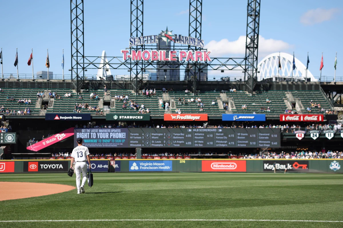 Kade Anderson walks on the field at T-Mobile Park. He wears a white Mariners uniform and a blue cap.
