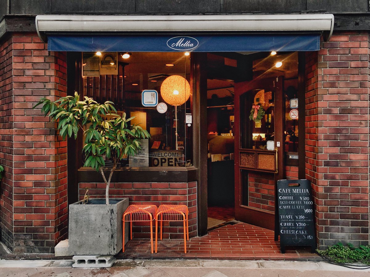 wrathofgnon's tweet photo. In Japan you will often see cafes and small shops with a small triangle shaped entrance cut into the front of the shop. The purpose is to soften the abrupt difference between shop interior and outside street and give customers a sheltered spot to sort out their umbrellas etc. It looks instantly welcoming and intimate. Here is a cozy cafe in Tokyo. The two chairs outside are for customers to wait their turn outside if the cafe is full. This is a tiny example of #GoodUrbanism on narrow streets and making the most of otherwise bland straight shop fronts.